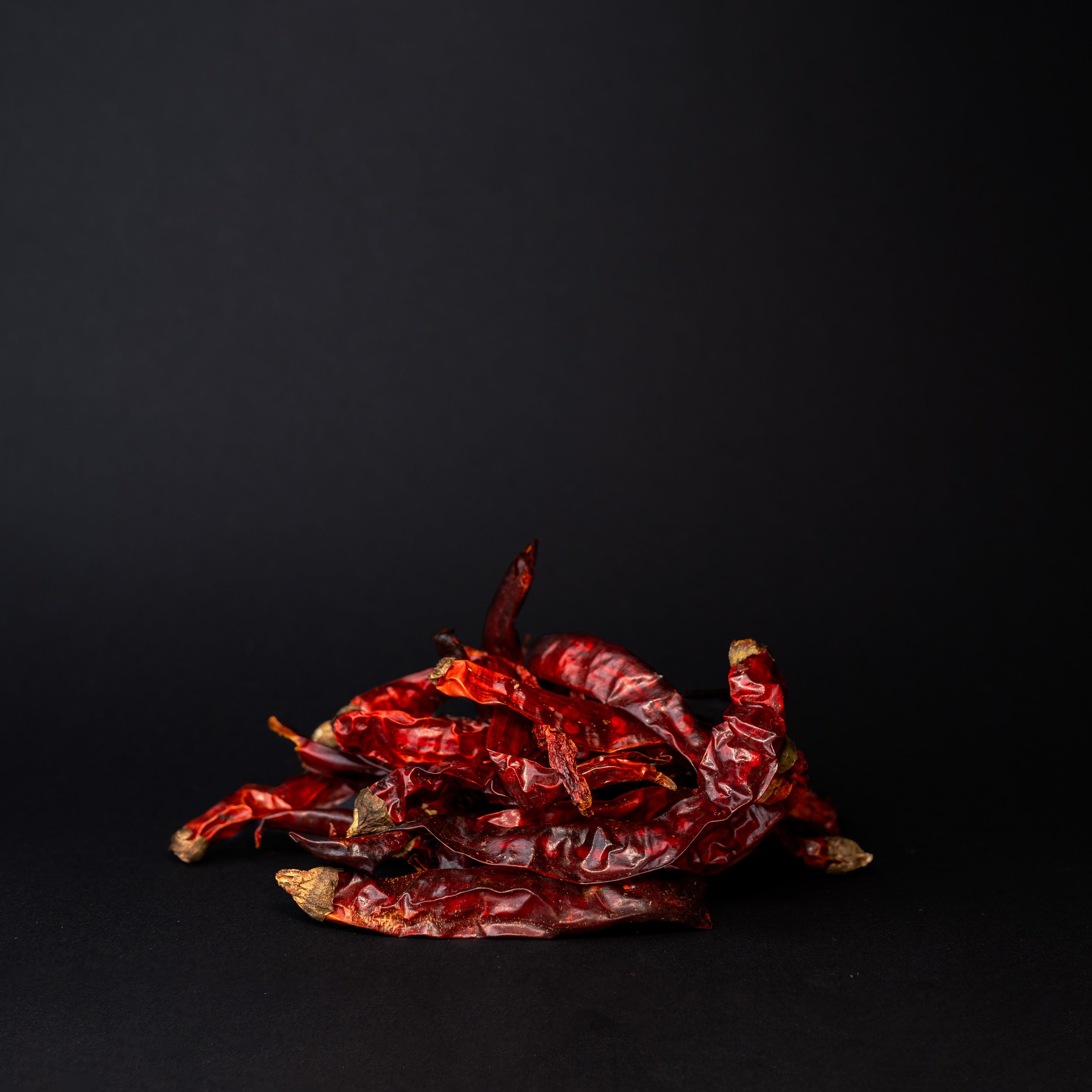 A pile of er jing tiao chili peppers on a black background. 
