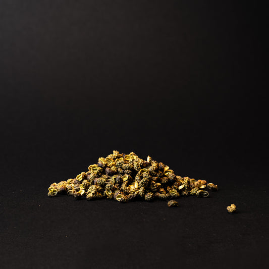 A small pile of green Sichuan peppercorns on a dark background.